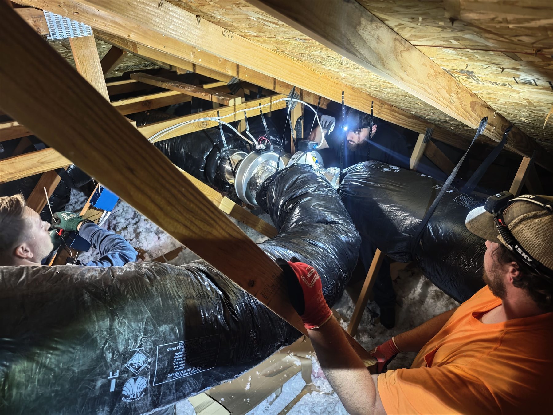 Technicians installing insulated attic ductwork in a residential attic space