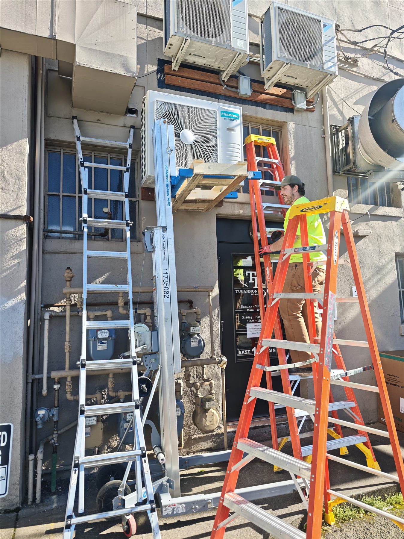 Banana Mechanical technician installing elevated heat pump equipment on a commercial exterior wall