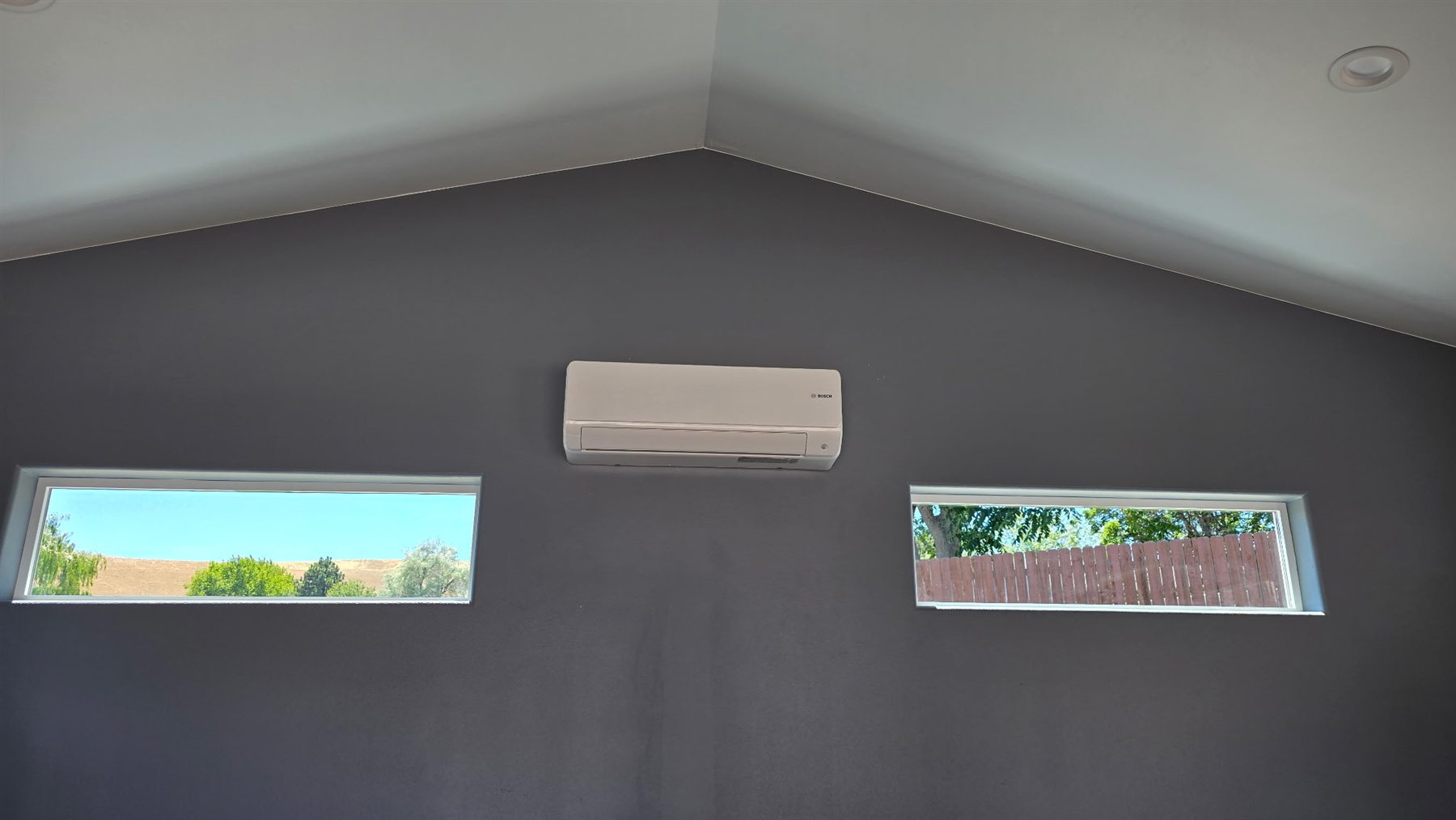 Indoor Bosch mini-split head mounted high on a gray wall between windows