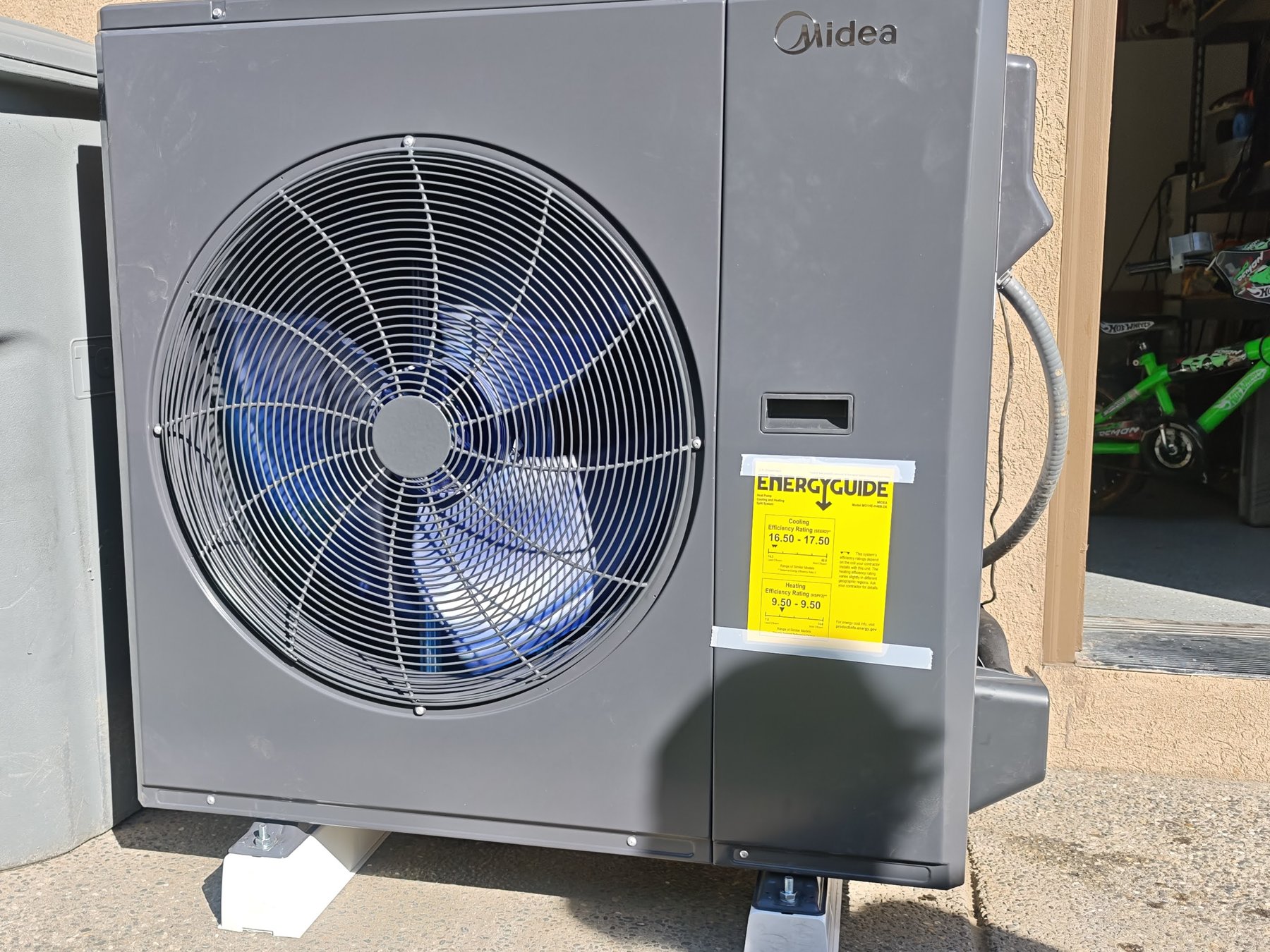 Midea outdoor heat pump condenser installed beside a residential garage