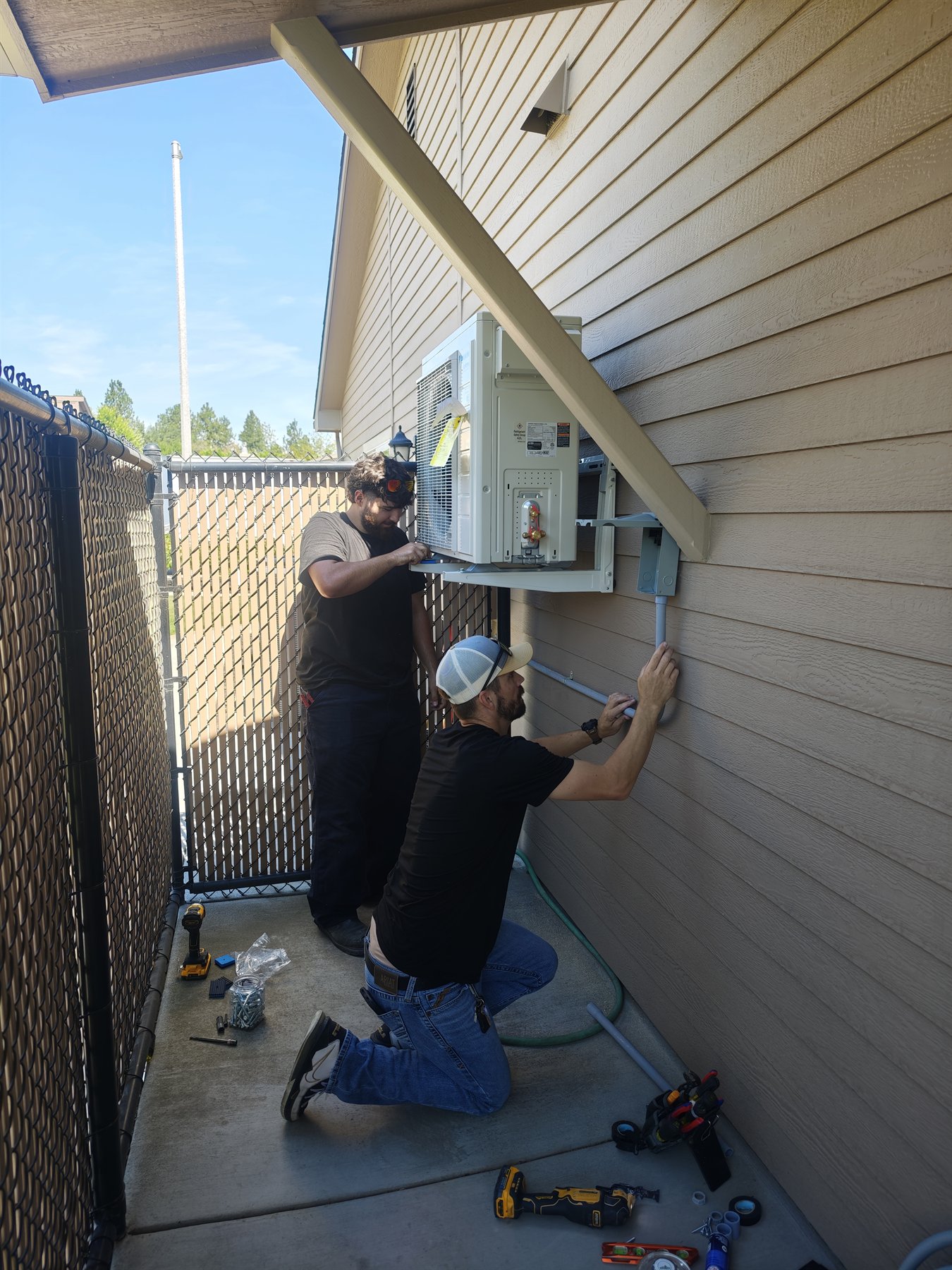 Banana Mechanical technicians installing a wall-mounted outdoor mini-split condenser