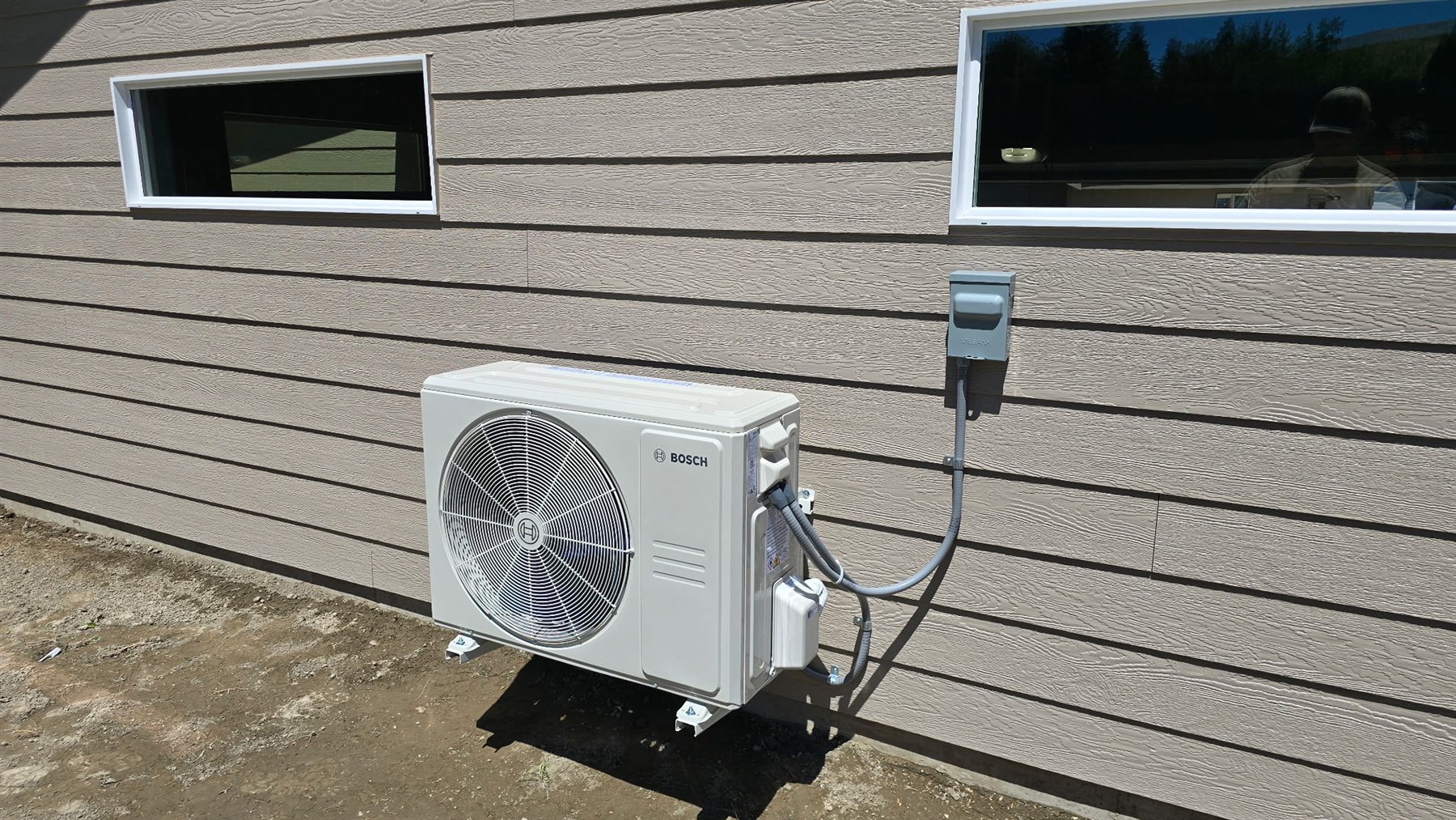 Outdoor Bosch heat pump condenser installed beside a home with electrical disconnect and conduit