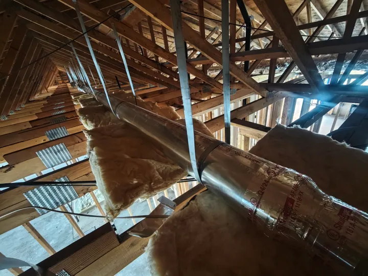 Commercial apartment HVAC ductwork routed through open attic framing during rough-in